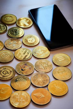 Dijital yatırım ve finansal teknolojiyi sembolize eden çeşitli altın renkli kripto para birimlerinin yanında bir akıllı telefon bulunuyor..