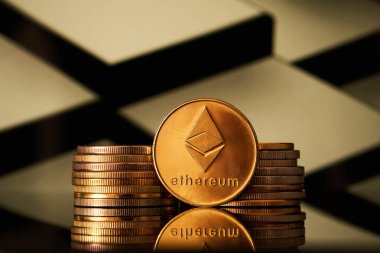 Arka planda geometrik deseni olan bir yüzeye yansıyan birçok altın ethereum kripto para birimleri bir yığın içinde düzenlenmiştir..