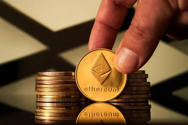 Arka planda geometrik deseni olan bir yüzeye yansıyan birçok altın ethereum kripto para birimleri bir yığın içinde düzenlenmiştir..