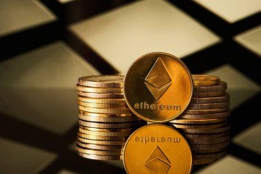Arka planda geometrik deseni olan bir yüzeye yansıyan birçok altın ethereum kripto para birimleri bir yığın içinde düzenlenmiştir..