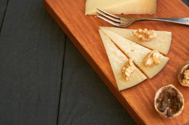 Ahşap bir tahta, ceviz yarısıyla dilimlenmiş peynirleri sergiler. Atıştırmalık ya da toplayıcılık için mükemmel bir davet sunar..