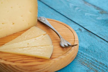 Dairesel ahşap bir tahta küçük bir çatalın yanında birkaç dilim peynir tutar. Canlı mavi masa ortama kırsal bir cazibe katıyor, aperatif ya da aperatif için mükemmel..