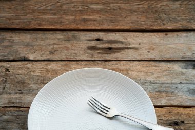 Basit bir beyaz tabak yıpranmış ahşap bir masada oturur, kenarında duran gümüş bir çatalla birlikte, sahanın kırsal cazibesini vurgular..