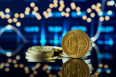 Altın renkli XRP kripto para birimi yansıtıcı bir yüzeyde istiflenmiş sikkelerle çevrili, arka planda canlı pazar eğilimi çizgileri var, dijital para birimi manzarasını gösteriyor.