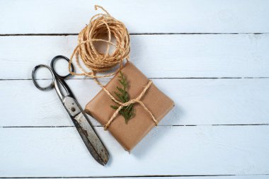 Dikkatlice paketlenmiş bir hediye, bir makas eşliğinde iple bağlanır. Kırsal ahşap arka plan sunumun büyüleyici, el yapımı estetiğini güçlendirir..
