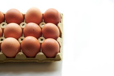 Taze kahverengi yumurtalar bir yumurta kutusuna yerleştirilir, pürüzsüz yüzeyleri ve doğal renkleri parlak beyaz arka planda sergilenir. Yumurtalar temiz bir görünüm elde etmek için dikkatlice düzenlenmiştir..