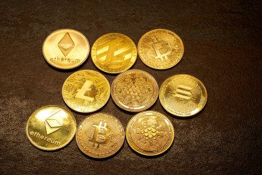 Farklı kripto para birimlerinden oluşan bir koleksiyon, popüler dijital para birimlerinin tasarımları ve logolarını gösteren koyu dokulu bir yüzeye yakın bir şekilde düzenlenmiştir..