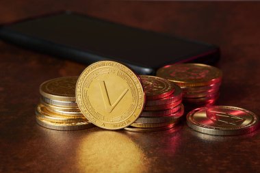 Vethor cryptocurrency surrounded by more cryptocurrencies spread out on a dark wooden table next to a smartphone, highlighting the growing interest in digital finance. clipart