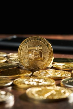 Parlak kripto para koleksiyonu ahşap bir masa üzerine yayılmış, Binance madeni para açıkça ortada görünür, çevre ışığı altında parlayan.
