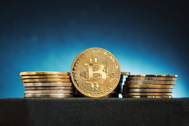 Parlak Bitcoin para yığınları, mavi ışıkla aydınlatılmış bir yüzeyde sanatsal olarak düzenlenir. Karmaşık detaylarını gözler önüne serer ve modern bir finansal çağı yansıtır..