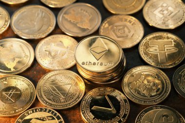 Karanlık bir yüzeyde çeşitli kripto para birimleri sergileniyor, Ethereum vurgulanıyor, karmaşık tasarımlar ve logolar sergileniyor, dijital finans piyasasının artan popülaritesini yansıtıyor.