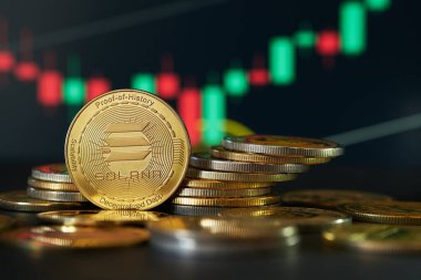 Bir yığın önünde bir Solana madeni para, arka planda değer dalgalanmalarını gösteren bir fiyat tablosu.