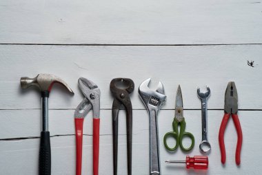 Bir çekiç, anahtar ve kerpeten de dahil olmak üzere el aletleri koleksiyonu beyaz ahşap bir yüzey üzerinde sergileniyor, DIY projeleri ve onarımlara hazır..