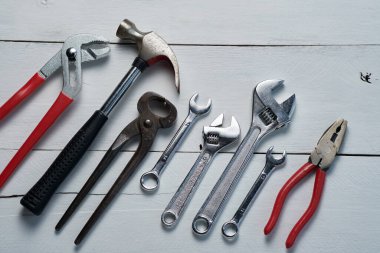 Bir çekiç, anahtar ve kerpeten de dahil olmak üzere el aletleri koleksiyonu beyaz ahşap bir yüzey üzerinde sergileniyor, DIY projeleri ve onarımlara hazır..