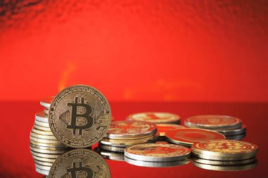 Parlak bitcoin paralarının bir koleksiyonu yansıtıcı bir yüzeye oturur, canlı kırmızı bir zemin ile aydınlatılır, kripto para biriminin değerini ve cazibesini vurgular..