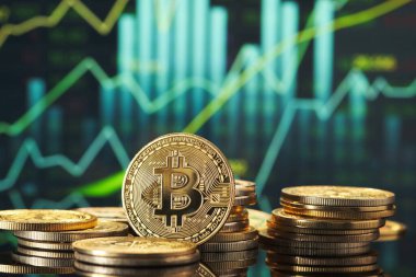 Altın Bitcoin sikkeleri, pazar eğilimlerini ve kripto para dalgalanmalarını modern bir ortamda temsil eden yeşil ve mavi finansal grafikler önünde sergilenmektedir..