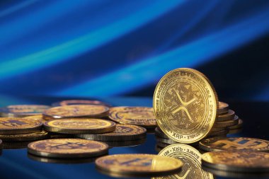 Parlak bir yüzeye yayılmış altın Xrp kripto para birimleri. Arkaplanda şifreli para birimi temasını vurgulayan canlı bir mavi dijital kalıp yer alıyor..