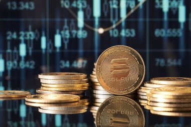 Altın Solana sikkeleri, pazar eğilimlerini ve kripto para dalgalanmalarını modern bir ortamda temsil eden yeşil ve mavi finansal grafikler önünde sergilenmektedir..