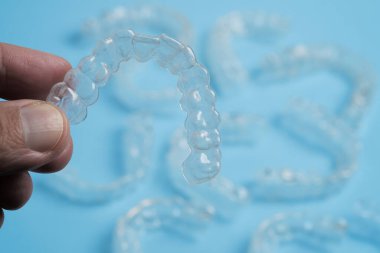 Bazıları açık mavi arka planda dinlenirken bir el temiz bir diş hizalayıcısını tutar. Bu düzenek diş düzeltmeye modern yaklaşımı sergiliyor.