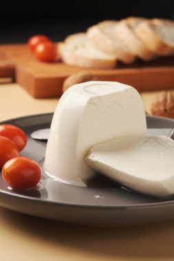 Bir kalıp peynirin yanında dilimlenmiş ekmek, taze vişneli domates ve gri tabakta bütün ceviz. Ayarlama basit bir kırsal atıştırmanın altını çiziyor..