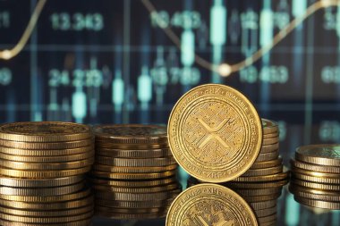 Altın XRP sikkeleri, pazar eğilimlerini ve kripto para birimlerindeki dalgalanmaları temsil eden yeşil ve mavi finansal grafikler önünde modern bir ortamda sergilenmektedir..