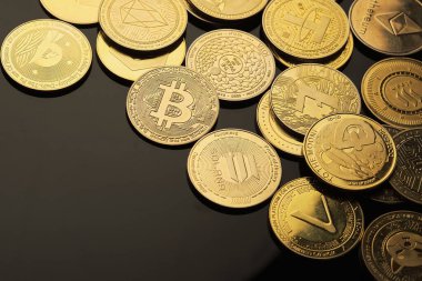 Farklı kripto para birimlerine sahip çeşitli koleksiyonluk paralar siyah yansıtıcı bir yüzey üzerinde düzenlenir, karmaşık tasarımlar ve logolar sergilenir..