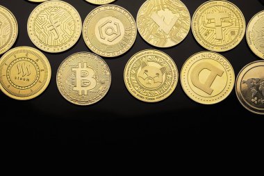 Farklı dijital para birimlerini temsil eden birçok ikonik dizayn ve sembollerin gösterildiği siyah bir yüzey üzerinde çeşitli kripto para birimleri sergilenmektedir..