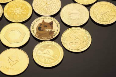 Farklı kripto para birimlerine sahip çeşitli koleksiyonluk paralar siyah yansıtıcı bir yüzey üzerinde düzenlenir, karmaşık tasarımlar ve logolar sergilenir..