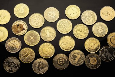 Farklı dijital para birimlerini temsil eden birçok ikonik dizayn ve sembollerin gösterildiği siyah bir yüzey üzerinde çeşitli kripto para birimleri sergilenmektedir..