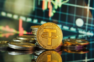 Bağlı dijital para birimleri yansıtıcı bir yüzeye yığılmış ve arka planda bir ticaret tablosu var. Sahne, kripto para ticaretinin ve yatırımın özünü yakalıyor..