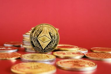 Altın Ethereum kripto para birimlerinden oluşan bir koleksiyon parlak kırmızı bir arkaplanda belirgin bir şekilde sergilenmektedir. Sikkeler dijital para birimi kavramlarını temsil ediyor ve finans ve yatırımı vurguluyor.