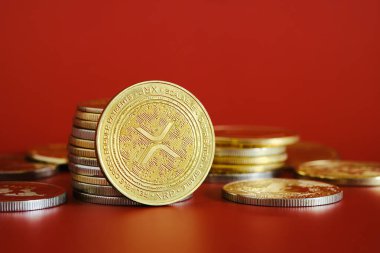 Altın bir XRP kripto para koleksiyonu parlak kırmızı bir arkaplanda belirgin bir şekilde sergilenmektedir. Sikkeler dijital para birimi kavramlarını temsil ediyor ve finans ve yatırımı vurguluyor.