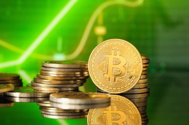 Bitcoin sikkeleri, piyasa eğilimlerini ve kripto para dinamiklerini sembolize eden canlı yeşil bir finansal grafikle tezat oluşturan yansıtıcı bir yüzeye istiflenmiştir..