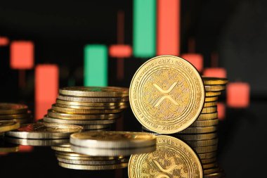 Piyasa eğilimleri ve dalgalanmaları gösteren canlı bir ticaret grafiğinin zeminine karşı, çeşitli XRP kripto para birimleri yığınlar halinde düzenlenmiştir, ışığı yansıtır.