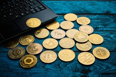 Farklı kripto para birimleri, parlak mavi ahşap bir masada siyah bir dizüstü bilgisayarın yanına yayılır. Sahne, rahat bir ortamda dijital para birimini vurguluyor.