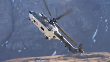 Dar bir dağ vadisinde yüksek hızda uçan askeri helikopter, parlak ve güneşli bir günde yanaşır ve işaret fişeği atar. Ebenfluh atış poligonunda İsviçre Hava Kuvvetleri 'nden Eurocopter AS532 Cougar