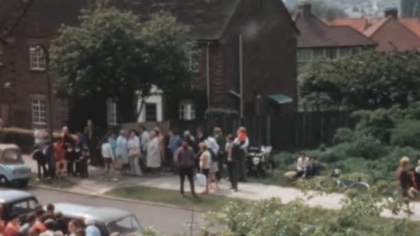 通りに車が停まっている歴史的な家の外で待っている観光客のグループ 1970年イギリス — ストック動画