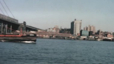 A massive ship sailing under the iconic Brooklyn Bridge. Gliding along the East River with the New York City skyline visible in the distance. Vintage footage of 1960s.
