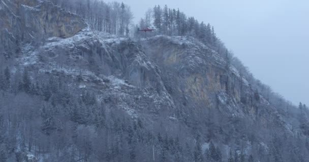 直升机运送的原木绑在一个带陡峭积雪覆盖高山背景的中心钩上的绳子上 Kaman Max Zpo型直升机 配有啮合转子 同步变色器 — 图库视频影像