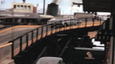 Car driving down a curved bridge showcasing Niagara Falls, New York seaport and chimney with smoke in the background. Rare vintage footage of the 1960s.