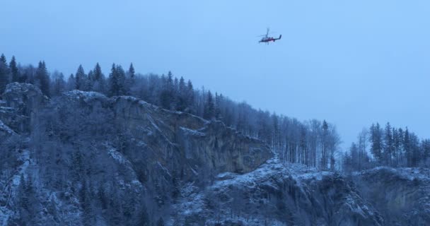 Hubschrauber Schweben Der Nähe Eines Schneebedeckten Berges Mit Einem Wald — Stockvideo