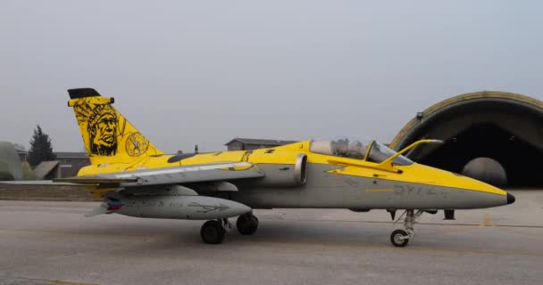 戦闘機の黄色の尾に黒で描かれたインディアンインディアン戦士の肖像画 空港滑走路に課税されるイタリア空軍のAmxジブリ — ストック動画