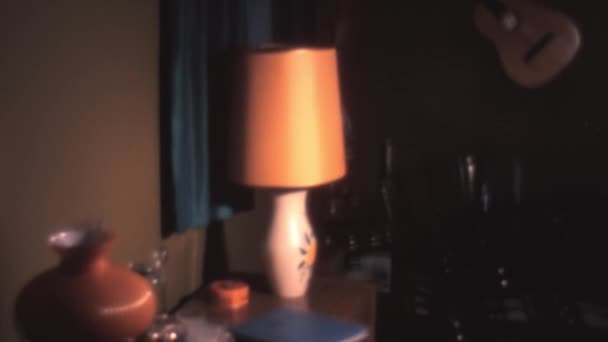 薄暗い照明の部屋のランプの下の茶色の側のテーブルの上に青い写真アルバムがあります 70年代からニューヨークアメリカのアパートのインテリア — ストック動画