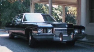 1970 'lerden kalma büyük siyah lüks Amerikan arabası bir villanın yanına park edilmiş. Cadillac Fleetwood, Washington D.C. kırsalında güneşli bir günde. Ön görünüm.