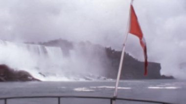 Kanada Bayrağı Bayrak Direğinde Dalgalanıyor. Bulutlu Gün 'de Niagara Şelalesi Arkaplanı. Dramatik 1970 'lerin Arşiv Görüntüsü Super mm Film Reel' den Dijital.