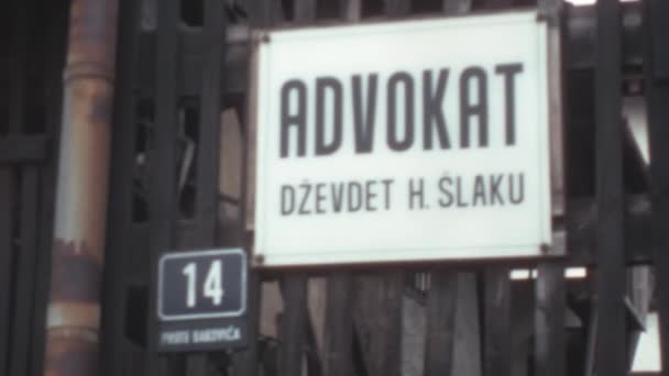 建物の鉄の入り口のドアからぶら下がっている白い背景に黒い文字Adovokat Dzevdet Slakuで看板の終わります サラエヴォのバコビカ通りStari Grad 1970年ボスニア — ストック動画