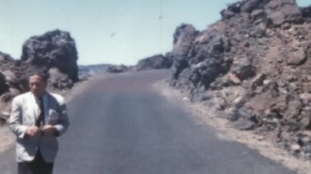 男は道路を歩き スペインのハゲワシの下でテネリフェ島の植物の匂いを嗅いでいますデルTeide 1955年にラス カナダで風が吹く美しい晴れた日 美しい背景風景 — ストック動画
