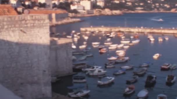 1970年代にドゥブロヴニク クロアチアの古い観光都市の港が歩いていた ターコイズの海に浮かぶ小さなボート ユーゴスラビアのアーカイブ映像 — ストック動画