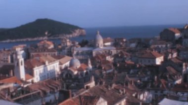 1970 'lerde Hırvatistan' ın Dubrovnik kentindeki açık mavi gökyüzüne karşı Roma katedrali ve küçük kırmızı çatılı evleri olan eski bir şehrin panoraması.