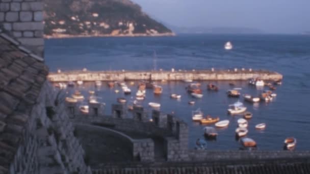 20世纪70年代 从中世纪城墙顶上俯瞰克罗地亚杜布罗夫尼克古城港口的空中景观 小船停泊在碧绿的水面上 — 图库视频影像